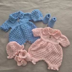 May include: Two knitted baby rompers with matching bonnets and booties. One set is light blue with a textured diamond pattern, a collared neckline, and two wooden buttons. The other set is pale pink with a similar textured pattern and buttons.