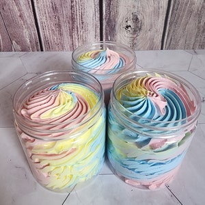 May include: Three glass jars filled with whipped body butter. The butter is swirled in shades of pink, yellow, and blue.