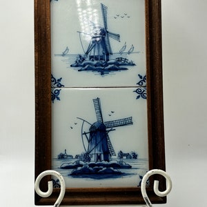Peut inclure: Deux images de moulins à vent en faïence Delft bleue et blanche dans des cadres en bois sur un chevalet en métal blanc.