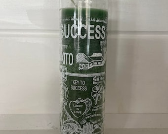 May include: Green glass candle with white text that reads "SUCCESS" and "KEY TO SUCCESS". The candle also has images of hearts, four-leaf clovers, money, and other symbols related to good luck and prosperity.