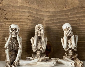 May include: Three white skeletal figures in a seated pose, each covering their eyes, ears, and mouth. The figures are a representation of the "See no evil, hear no evil, speak no evil" proverb.