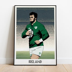 May include: A black and white illustration of a rugby player in a green jersey and white shorts holding a rugby ball. The player is standing on a green field with a stadium in the background. The text "IRELAND" is printed below the player.