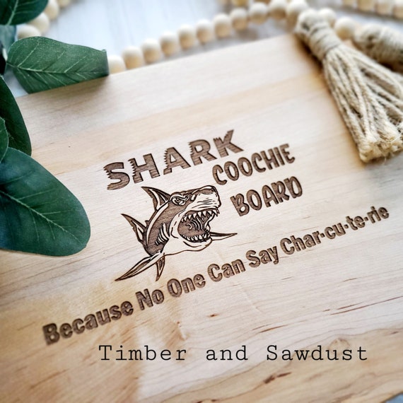 The 'Shark Coochie Board' name alone is a conversation starter — a punny, engraved cutting board that roasts anyone who calls it a charcuterie board.