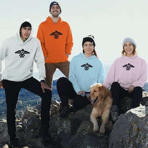 May include: Four people wearing hoodies with a black geometric bird design. The hoodies are in white, orange, light blue, and pink. A golden retriever dog is sitting in front of them.