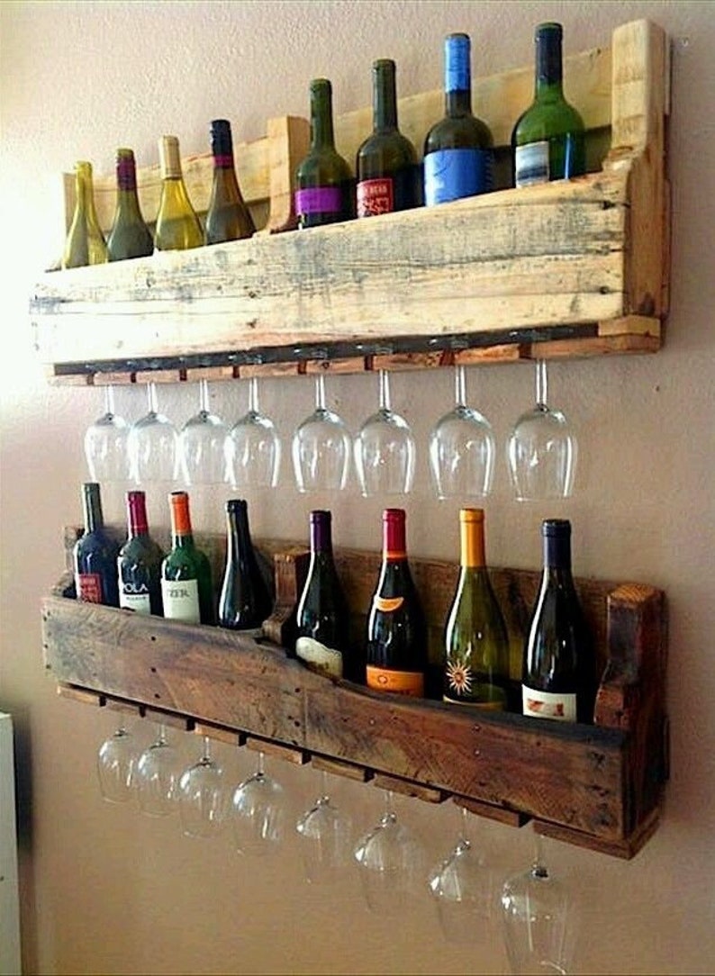 May include: A rustic, two-tiered wooden wine rack with space for wine bottles and hanging wine glasses. The rack is made from reclaimed wood and has a natural, weathered appearance. The rack holds various wine bottles and clear wine glasses.