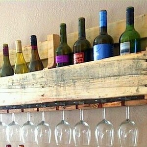 May include: A rustic wooden wine rack with a shelf for wine bottles and a row of hanging wine glasses. The rack is made from reclaimed wood and holds several wine bottles of various colors and sizes. The wine glasses are clear and stemless.