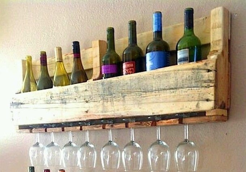 May include: A rustic wooden wine rack with a shelf for wine bottles and a row of hanging wine glasses. The rack is made from reclaimed wood and holds several wine bottles of various colors and sizes. The wine glasses are clear and stemless.