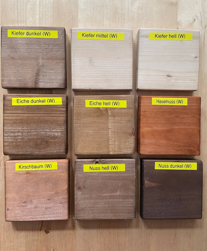 May include: Nine wooden blocks with different wood stain colors, including dark, medium, and light tones. Each block has a yellow label with German text. The colors range from light beige to dark brown.
