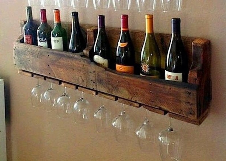 May include: A rustic wooden wine rack with a dark finish, holding several wine bottles and clear wine glasses. The rack is mounted on a wall, showcasing a collection of various wine types.