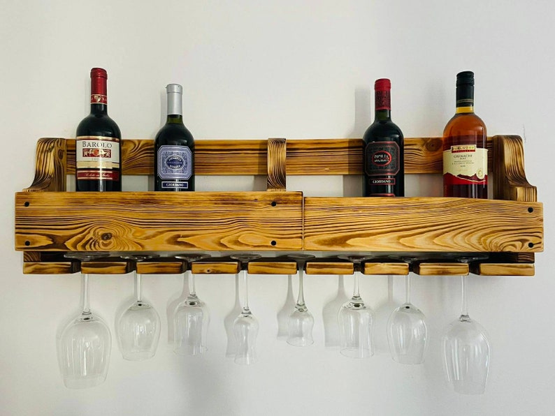May include: A rustic, wooden wine rack with a natural finish, holding four wine bottles and eight wine glasses. The rack is mounted on a white wall, showcasing the bottles and glasses.