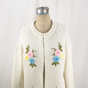 White acrylic knit vintage cardigan with hook and eye closure at neck and puffy embroidered flowers at top and each bottom corner.