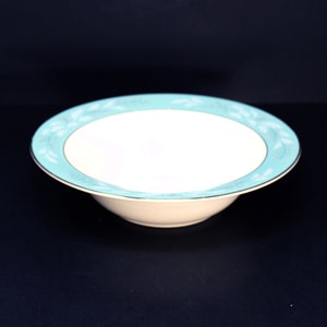 May include: A white ceramic bowl with a turquoise rim and a white floral design. The bowl is on a black background.