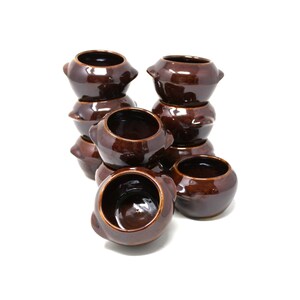 May include: A stack of eight brown ceramic pots with rounded edges and handles. The pots are arranged in a pyramid shape.