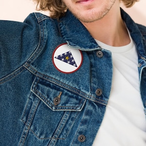 May include: A blue denim jacket with a white and blue folded flag patch on the left side of the chest.