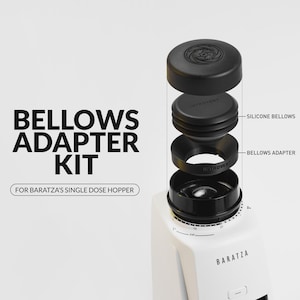 May include: A black Bellows Adapter Kit for Baratza's single dose hopper. The kit includes a black lid, silicone bellows, and a bellows adapter. The white Baratza grinder is visible at the bottom. Text on the image reads "Bellows Adapter Kit".