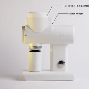 May include: A white coffee grinder with the text "sculptor..." and labels for "INTROVERT Single Dose Hopper + Bellows" and "Stock Hopper." The grinder has a cylindrical base and a cup-like container below.