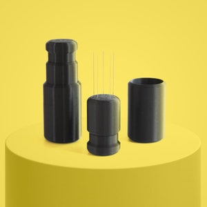 May include: Three black, cylindrical containers with a textured surface. The middle container has several thin, silver needles sticking out of the top.