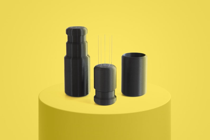 May include: Three black, cylindrical containers with a textured surface. The middle container has several thin, silver needles sticking out of the top.