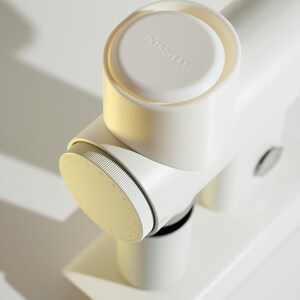 May include: A white, modern-looking device with the word "INTROVERT" on the top. The device has a cylindrical shape with a dial and a base. The design is minimalist and clean, with a focus on form and function.