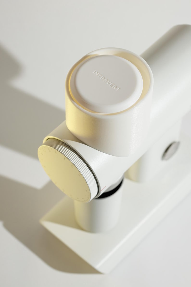 May include: A white, modern-looking device with the word "INTROVERT" on the top. The device has a cylindrical shape with a dial and a base. The design is minimalist and clean, with a focus on form and function.