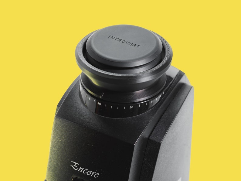 Pu&ograve; includere: Obiettivo per fotocamera nero con un tappo nero che dice "Introverso" su di esso. La fotocamera ha un quadrante con numeri da 20 a 30 e la parola "Encore" stampata sul lato.