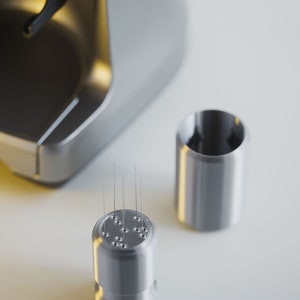 May include: Close-up of a silver coffee maker with a removable nozzle. The nozzle has multiple small holes and is designed for brewing coffee.