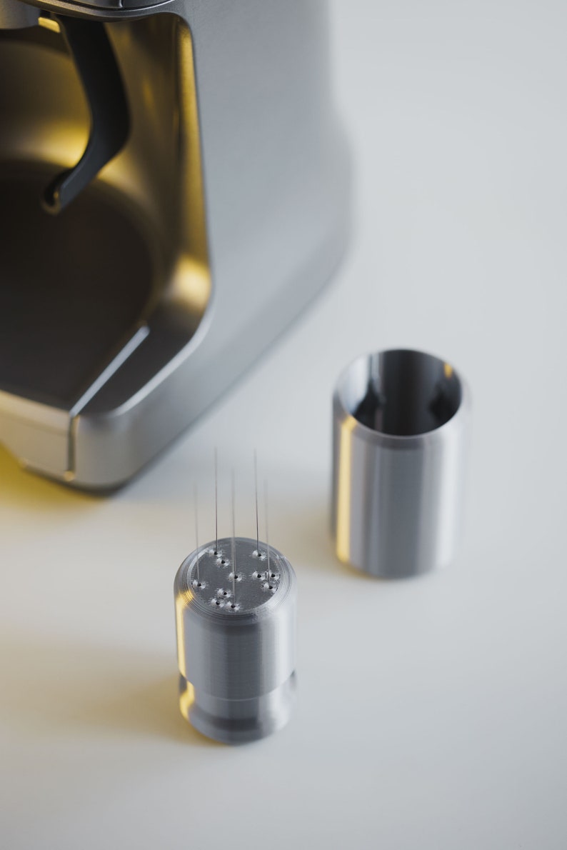 May include: Close-up of a silver coffee maker with a removable nozzle. The nozzle has multiple small holes and is designed for brewing coffee.
