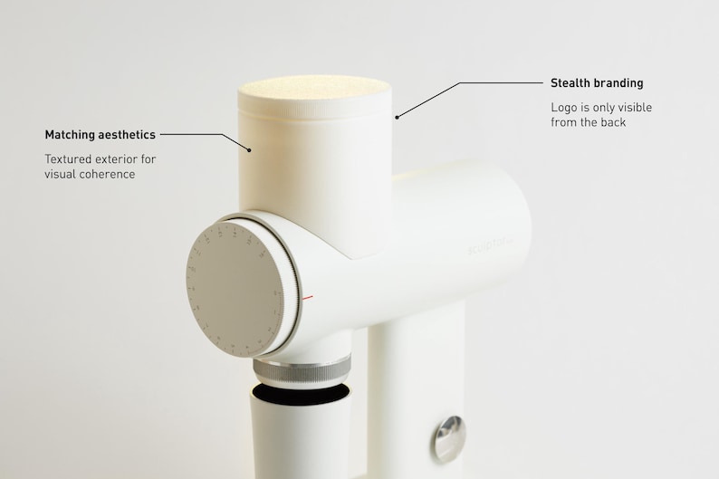 May include: A white kitchen appliance with a cylindrical design. It features a textured exterior for visual coherence and stealth branding, with the logo only visible from the back. The appliance has a dial with markings and a small, circular button.