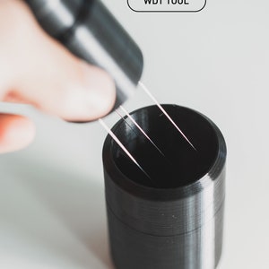 May include: A black 3D printed tool labelled "WDT TOOL" being used to insert four thin metal wires into a black 3D printed holder labelled "HOLDER".