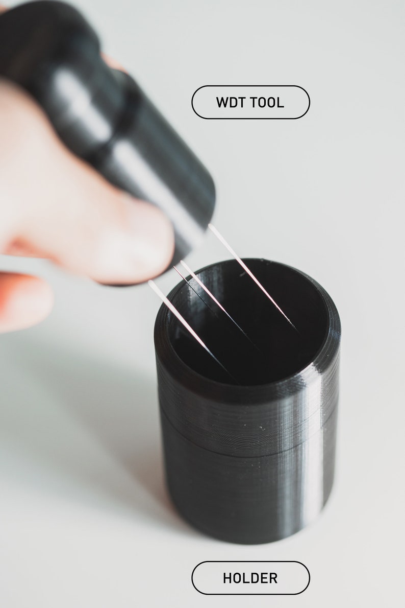 May include: A black 3D printed tool labelled "WDT TOOL" being used to insert four thin metal wires into a black 3D printed holder labelled "HOLDER".