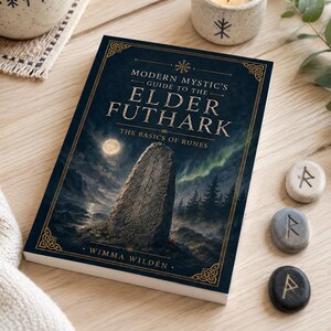 Könnte beinhalten: Ein Buch mit dem Titel "Modern Mystic's Guide to the Elder Futhark" mit dunkelblauem Einband, das eine Steinschnitzerei zeigt. Daneben befinden sich drei Runensteine, eine Tasse Tee, eine brennende Kerze und ein dekorativer Untersetzer. Autorin des Buches ist Wimma Wilden.