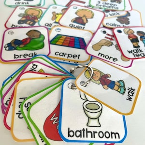May include: A set of colorful picture cards with various images and words, including "break", "carpet", "walk", "bathroom", "quiet", "more", "3 deep breaths", "calm", "all", "hands", "drink", "group", "sanitizer", and "kick". The cards are attached to a silver key ring.