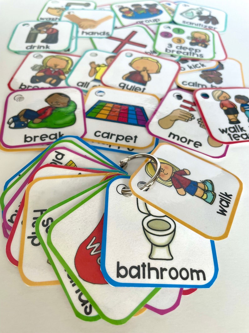 May include: A set of colorful picture cards with various images and words, including "break", "carpet", "walk", "bathroom", "quiet", "more", "3 deep breaths", "calm", "all", "hands", "drink", "group", "sanitizer", and "kick". The cards are attached to a silver key ring.