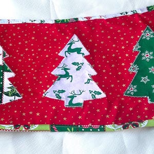 Puede incluir: Un camino de mesa navideño rojo con tres árboles de Navidad aplicados. Los árboles son blancos y verdes con varios diseños, incluyendo corazones, ciervos y copos de nieve. El camino de mesa mide unos 46 cm de largo.