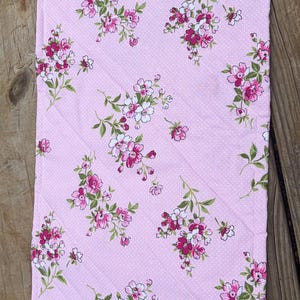 Op de afbeelding: Roze bloemenstof met witte stippen. De stof heeft een herhalend patroon van roze en witte bloemen met groene bladeren. De stof is gewatteerd met diagonale stiksels.