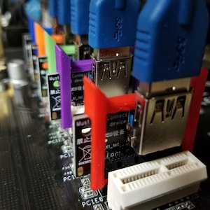 Puede incluir: Primer plano de una placa base de ordenador con varios puertos USB azules y plateados. Los puertos están etiquetados con el texto "AVA". Los puertos están rodeados de cubiertas de plástico de colores.