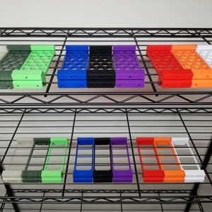 Op de afbeelding: Een set van 10 kleurrijke plastic opbergcontainers met een honingraatpatroon. De containers zijn gestapeld op een metalen plank.