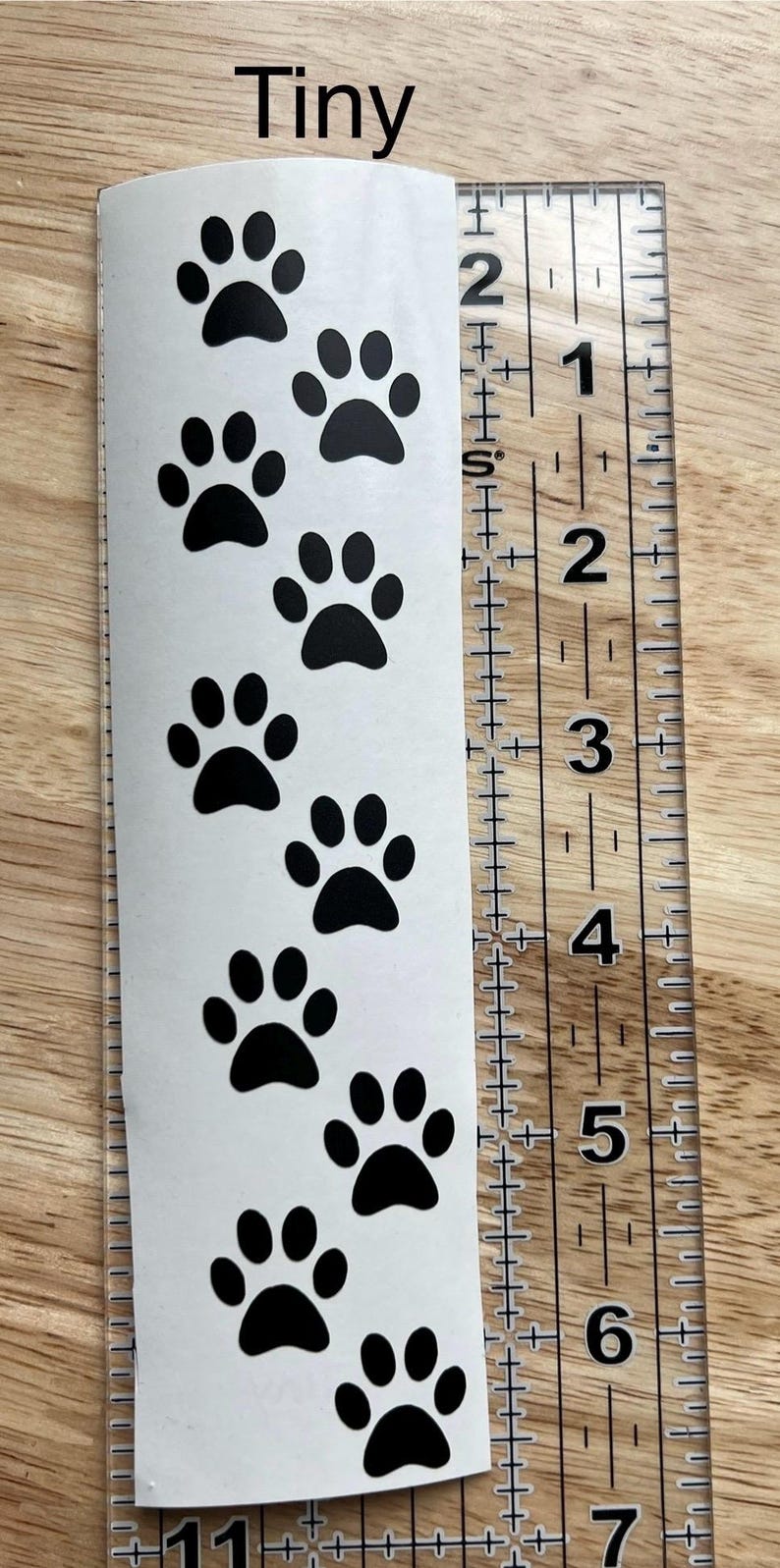 Puede incluir: Una tira adhesiva blanca con una serie de huellas de patas negras dispuestas en un sendero vertical. La palabra Tiny est&aacute; impresa en la parte superior. Una regla de pl&aacute;stico transparente est&aacute; junto al adhesivo, mostrando 16,5 cent&iacute;metros.