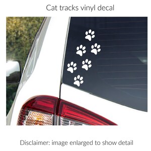 Puede incluir: Un adhesivo de vinilo blanco con un patr&oacute;n de seis huellas de gato aplicado en la ventana trasera de un veh&iacute;culo blanco. El texto Cat tracks vinyl decal aparece sobre la imagen y Disclaimer: image enlarged to show detail debajo.