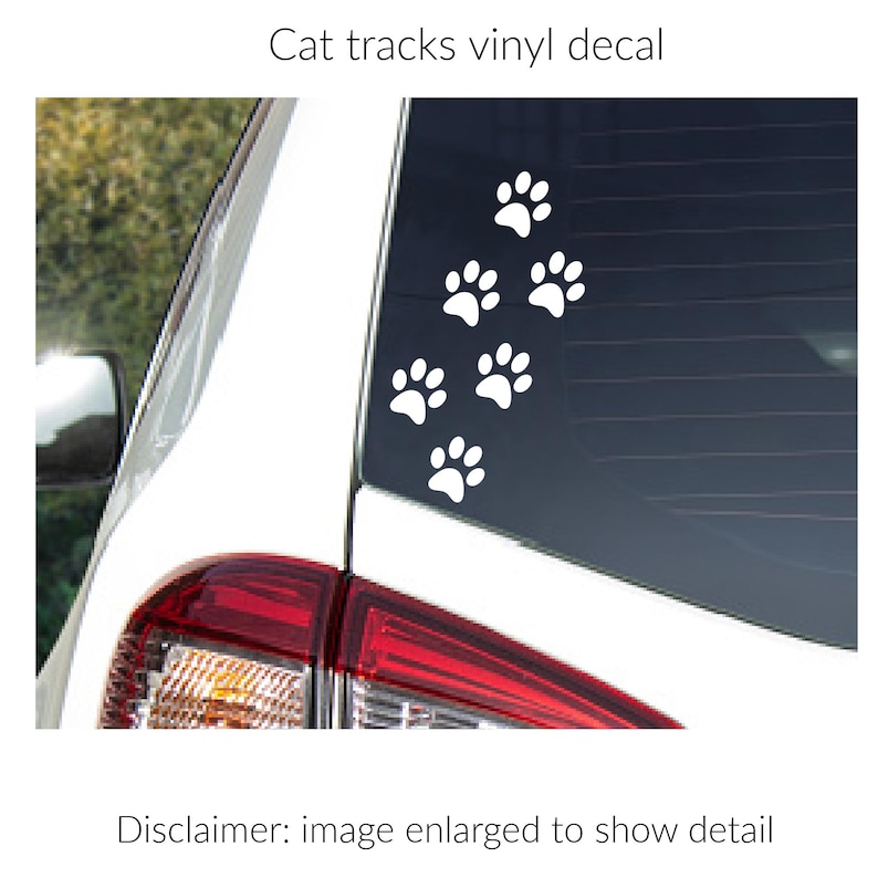 Puede incluir: Un adhesivo de vinilo blanco con un patr&oacute;n de seis huellas de gato aplicado en la ventana trasera de un veh&iacute;culo blanco. El texto Cat tracks vinyl decal aparece sobre la imagen y Disclaimer: image enlarged to show detail debajo.