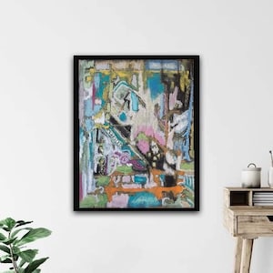 May include: Abstract painting in a black frame with a mix of colors including pink, blue, green, and orange. The painting is on a white wall with a desk and chair in the background.