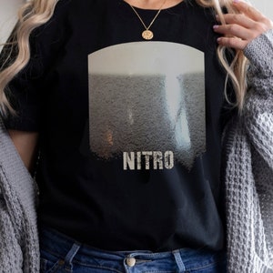 May include: Black t-shirt with a graphic of a glass of nitro cold brew coffee. The graphic is in shades of gray and white. The text "NITRO" is printed in white below the graphic.