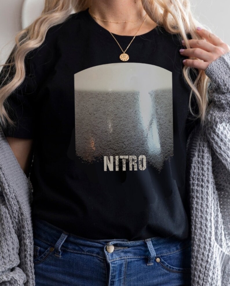 May include: Black t-shirt with a graphic of a glass of nitro cold brew coffee. The graphic is in shades of gray and white. The text "NITRO" is printed in white below the graphic.