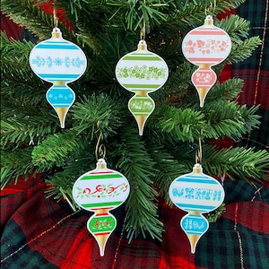 May include: A collection of five retro-style Christmas ornaments. Each ornament features a unique design with gold accents and a gold hanging loop. The ornaments are in various colors, including blue, green, and red, with floral and geometric patterns.