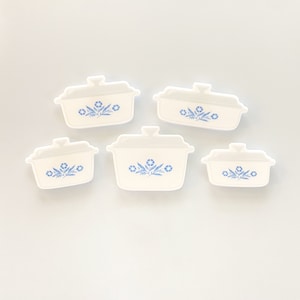 May include: Five white ceramic casserole dishes with blue floral designs. The dishes are arranged in a staggered pattern on a white background.