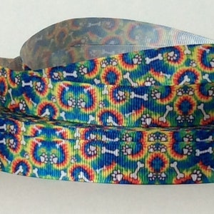 May include: A roll of colorful ribbon with a tie-dye pattern featuring paw prints and bone shapes. The ribbon is a bright blue, yellow, orange, and red.