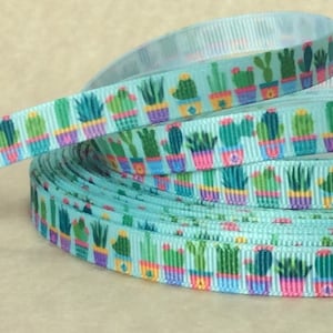 May include: A roll of turquoise blue ribbon with a repeating pattern of potted cacti in various shades of green, pink, and yellow.