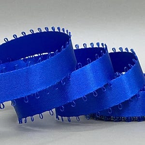 May include: A vibrant blue ribbon with a satin finish, featuring a delicate looped edge. The ribbon is coiled, showcasing its texture and sheen. Ideal for crafts, sewing, or gift wrapping.
