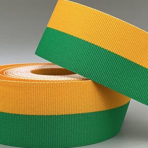 May include: A roll of yellow and green striped ribbon. The ribbon is made of a woven material and is rolled up in a coil. A length of the ribbon is unrolled and angled across the top of the coil.
