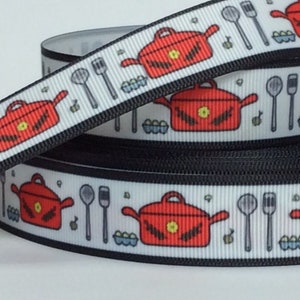 May include: White ribbon with a repeating pattern of red pots, kitchen utensils, and eggs. The ribbon is rolled up on a black spool.